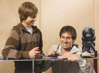 Germany, father and son fixing snowboard, smiling - WESTF11044