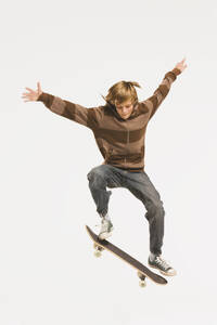 Jugendlicher (13-14) beim Sprung auf dem Skateboard, Arme ausgestreckt - WESTF11034