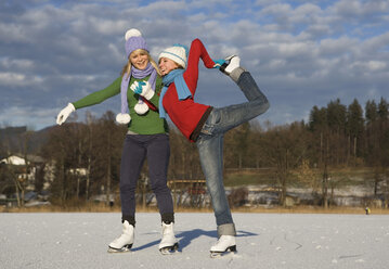 Austria, Salzkammergut, Lake Irrsee, Female teenagers (14-15) skating, one girl stretching leg - WWF00835