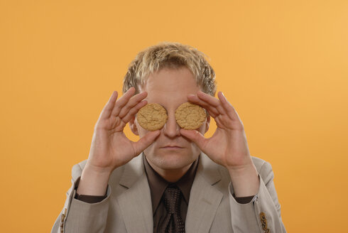 Businessman covering eyes with cookies, portrait - KJF00022