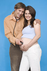 Mann hält Stethoskop auf den Bauch einer schwangeren Frau - RDF00950