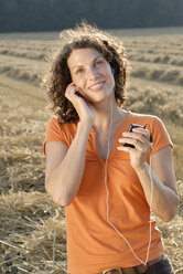 Junge Frau auf einem Feld, die einem MP3-Player zuhört, Porträt - KJF00048