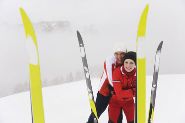 Italien, Südtirol, Paar in weinroter Kleidung, lächelnd, Skier im Vordergrund - WESTF11303