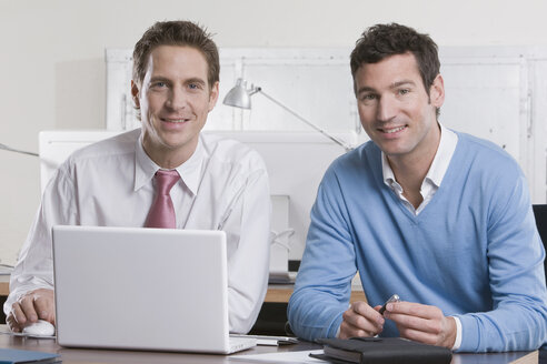 Deutschland, München, zwei Geschäftsleute im Büro mit Laptop, lächelnd, Porträt - LDF00663