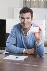 Germany, Munich, business man in office holding business card, smiling, portrait - LDF00640