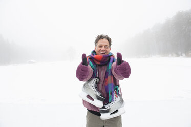 Italy, South Tyrol, Seiseralm, Man on frozen lake carrying ice skates, smiling, portrait - WEST11706