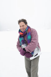 Italy, South Tyrol, Seiseralm, Man on frozen lake carrying ice skates, smiling, portrait - WEST11705