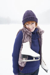 Italy, South Tyrol, Seiseralm, Young woman on frozen lake carrying ice skates, smiling, portrait - WEST11704