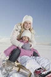 Germany, Bavaria, Munich, Mother and daughter (6-7) sitting on sledge, smiling, portrait - RBF00068