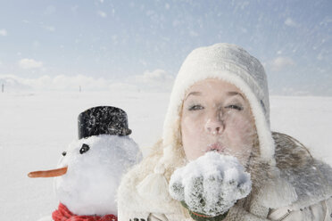 Deutschland, Bayern, München, Junge Frau bläst Schnee aus der Hand, Porträt - RBF00060