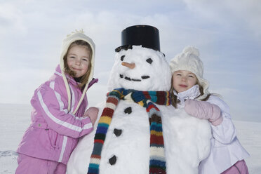 Germany, Bavaria, Munich, Two girls (4-5) (8-9) standing next to snowman, smiling, portrait - RBF00043