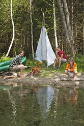 Österreich, Salzburger Land, Familie sitzt am Lagerfeuer am Wasser - HHF02922