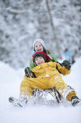 Germany, Bavaria, Siblings (8-9) sledding downhill, laughing - MAEF01757