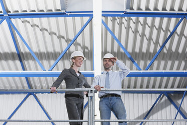 Germany, Neukirch, Man and woman architect standing in industrial hall, low angle view - WESTF11892