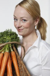 Young woman holding bunch of carrots, portrait - KSWF00508