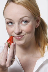 Young woman holding strawberry, smiling, portrait - KSWF00503