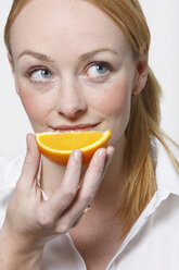 Young woman holding orange slice, portrait - KSWF00502