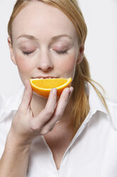 Young woman holding orange slice, eyes closed - KSWF00501