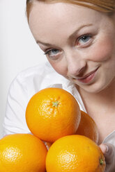 Young woman holding oranges, smiling, portrait - KSWF00500