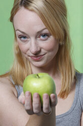 Young woman holding an apple, smiling, portrait - KSWF00497