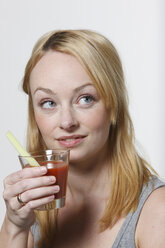 Young woman holding glass of tomato juice, portrait - KSWF00493