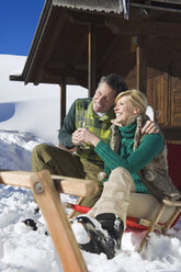 Italien, Südtirol, Seiseralm, Paar vor Blockhütte sitzend, Sektgläser haltend, lächelnd, Portrait - WESTF11439