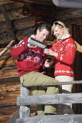 Italien, Südtirol, Seiseralm, Paar steht auf Deck einer Blockhütte, hält Thermoskanne - WESTF11354