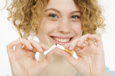 Young Woman breaking cigarette in half, smiling, portrait - CLF00833