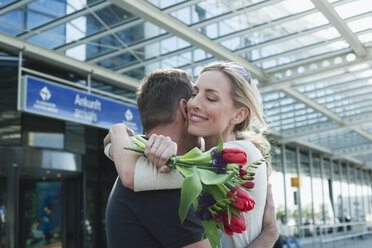 Deutschland, Leipzig-Halle, Flughafen, Pärchen umarmt sich, Frau hält Blumen - WESTF12100