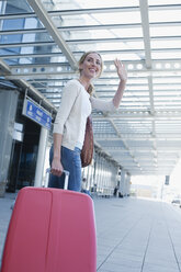 Germany, Leipzig-Halle, Airport, Young woman with suitcase, waving - WESTF12082