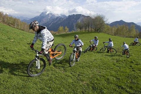 Italien, Comer See, Mountainbiker fahren über die Wiese, lizenzfreies Stockfoto