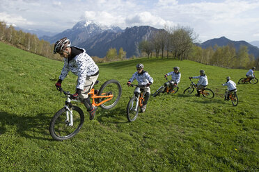 Italy, Lake Como, Mountain biker riding across meadow - FFF01070