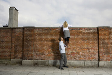 Germany, Bavaria, Munich, Young man helping young woman to climb a wall - RBF00089