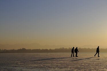 Deutschland, Bayern, Starnberger See, Silhouetten von drei Personen beim Schlittschuhlaufen - NHF01115