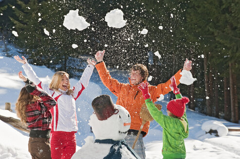 Österreich, Salzburger Land, Altenmarkt, Familie steht neben Schneemann, wirft Schnee in die Luft, lachend, Porträt - HHF02993