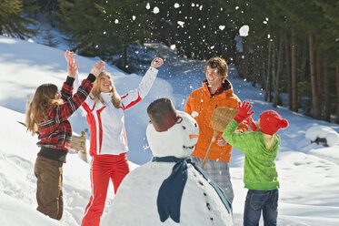 Österreich, Salzburger Land, Altenmarkt, Familie steht neben Schneemann, wirft Schnee in die Luft, lachend, Porträt - HHF02992
