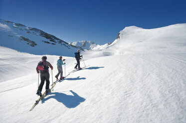 Austria, Salzburger Land, Altenmarkt, Zauchensee, Three persons cross country skiing in mountains, rear view - HHF02956