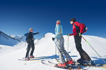 Österreich, Salzburger Land, Altenmarkt, Zauchensee, Drei Personen beim Skilanglauf in den Bergen, Mann zeigt mit Skistock - HHF02955