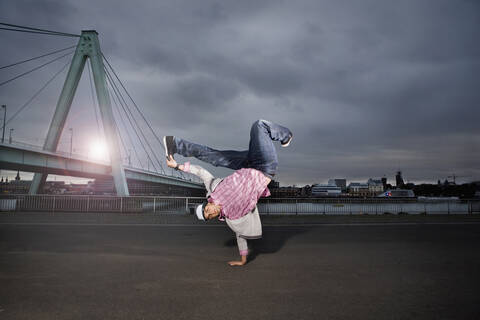 Deutschland, Köln, Junger Mann beim Breakdance, Rheinbrücke im Hintergrund, lizenzfreies Stockfoto