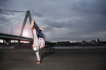 Germany, Cologne, Young man performing breakdance, Rhine bridge in background - SK00011