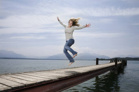 Deutschland, Chiemsee, Frau springt auf Steg, lizenzfreies Stockfoto