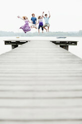 Germany, Bavaria, Ammersee, Four friends on jetty jumping in air - WESTF12225