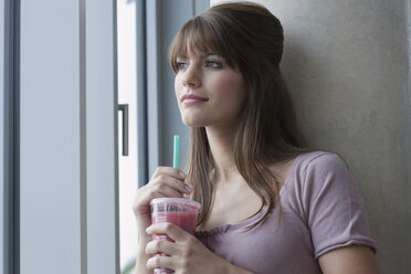 Germany, Cologne, Young woman holding plastic cup with drink, portrait - WESTF12411