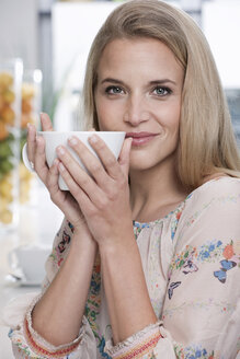 Germany, Cologne, Young woman in cafe holding a cup of coffee, portrait, close-up - WESTF12393