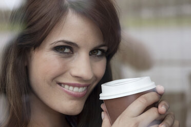 Germany, Cologne, Young woman holding plastic cup of coffee, smiling, portrait - WESTF12367
