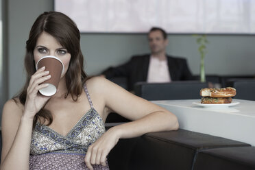 Deutschland, Köln, Junge Frau in Café trinkt Kaffee, Mann im Hintergrund - WESTF12355