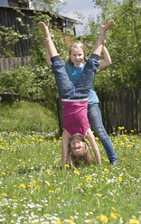 Österreich, Salzkammergut, Zwei Mädchen (10-11) im Garten, Mädchen hilft Freundin beim Handstand - WWF00971