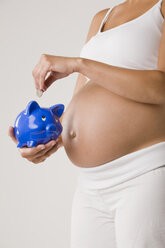 Schwangere Frau, die eine Euro-Münze in ein Sparschwein steckt, Mittelteil - LDF00700