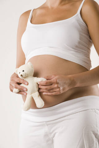 Schwangere Frau hält Teddy, Mittelteil, lizenzfreies Stockfoto