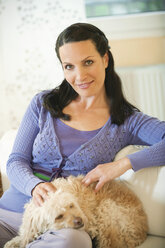 Frau sitzt auf einem Sofa mit Hund auf dem Schoß - WESTF12521